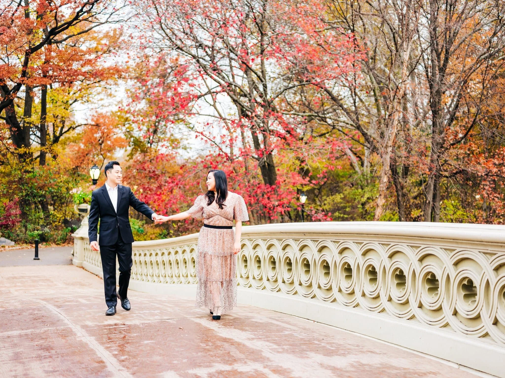 Engaged couple holding hands while walking across Bow Bridge during their Central Park engagement photo session in New York City.