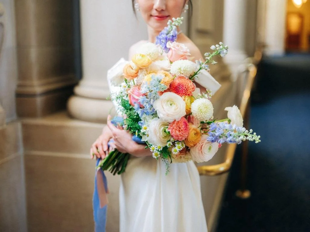 Close-up of a bridal bouquet with the bride partially visible behind the flowers.