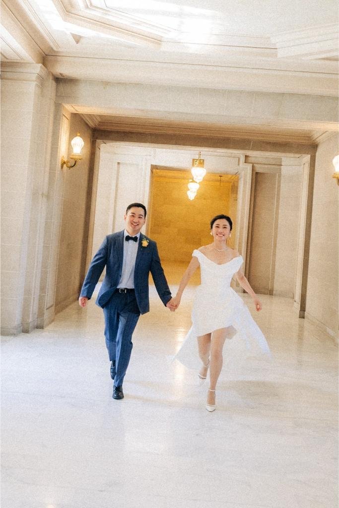 Bride and groom jogging hand in hand through a hallway at San Francisco City Hall.