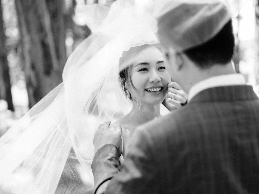 Groom gently touching the bride's face as her veil blows in the wind during portraits in the Presidio.