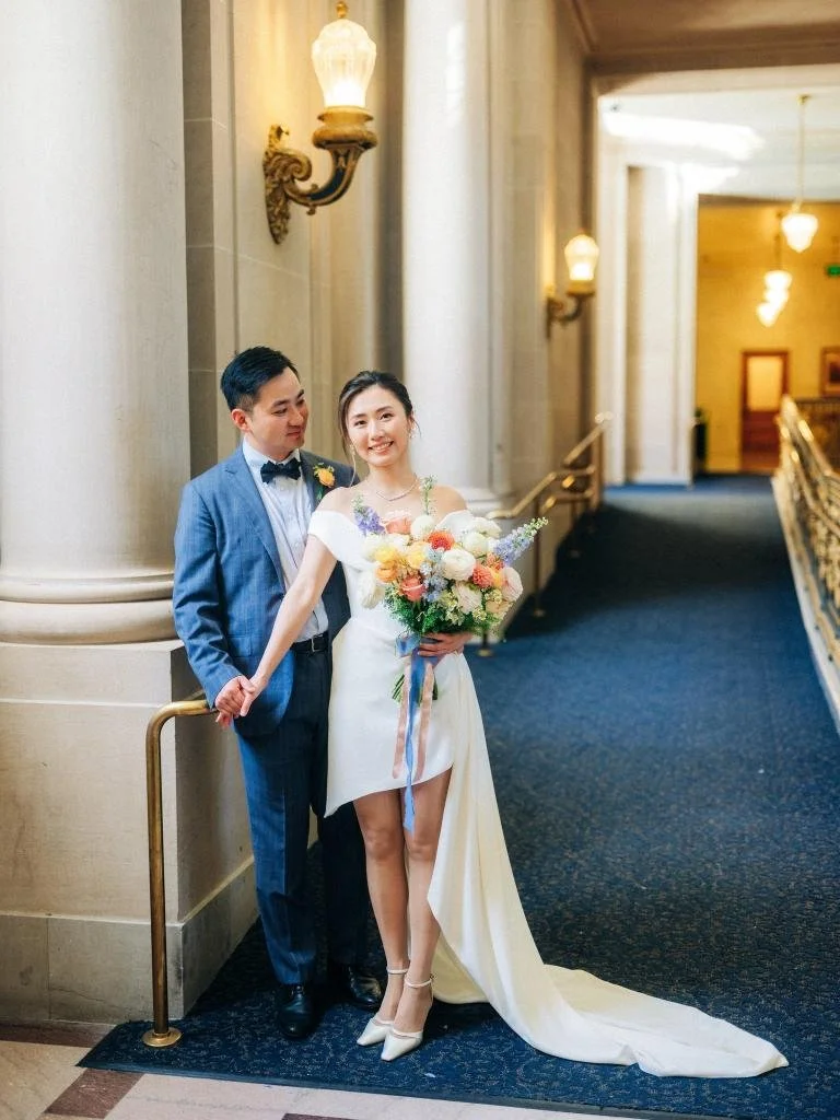 Groom standing behind the bride and holding her hand as she carries her wedding bouquet.