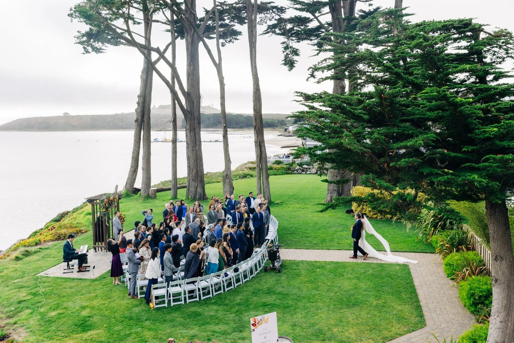 Wedding guests standing as bride walks down aisle during ceremony at Maverick’s Beach House in Half Moon Bay