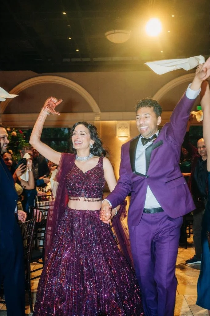 Bride and groom smiling with their hands raised as they enter the reception dining room