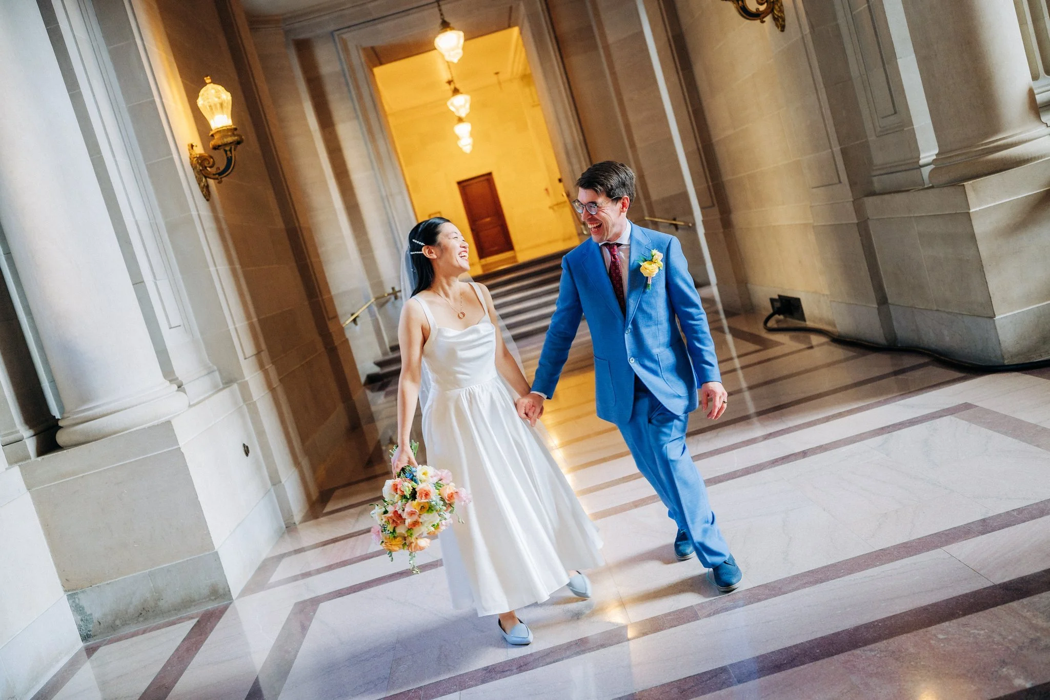 Bride and groom holding hands walking down hallway at San Francisco City Hall wedding