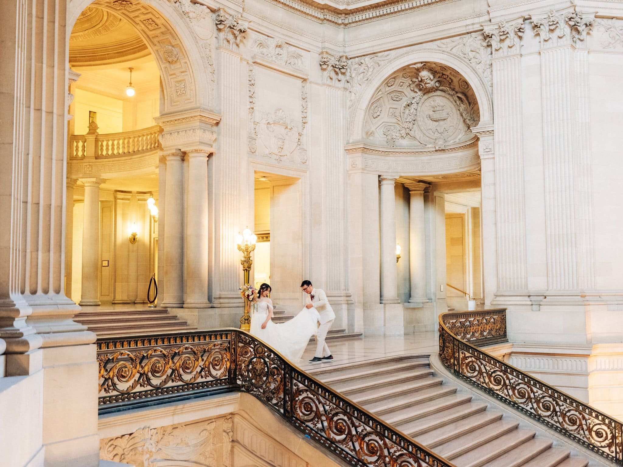 Groom lifting the bride’s dress at the top of the grand staircase during their San Francisco City Hall elopement.