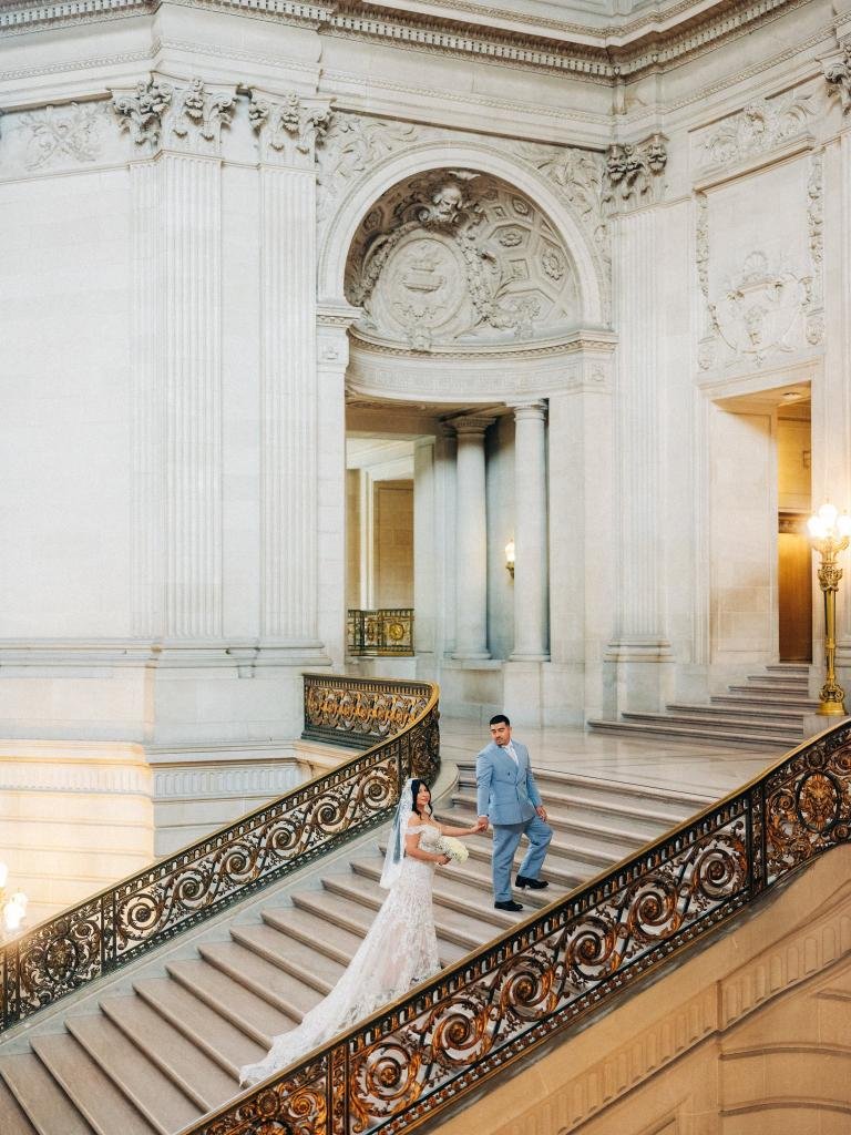 Groom looking back at bride while they hold hands near the top of the San Francisco City Hall staircase