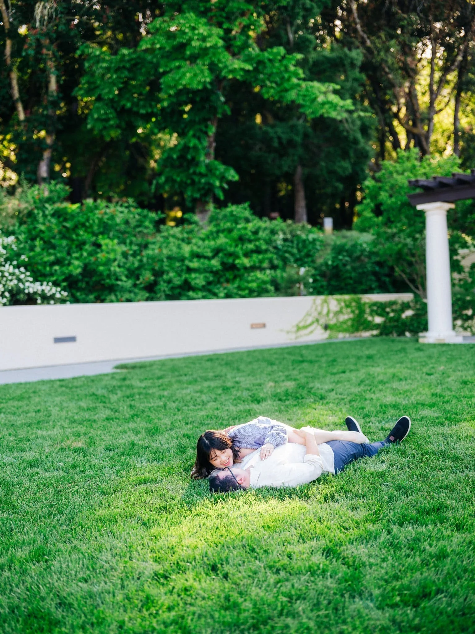 Couple laying on the grass and smiling at each other during their Montalvo Arts Center engagement photos in Saratoga.