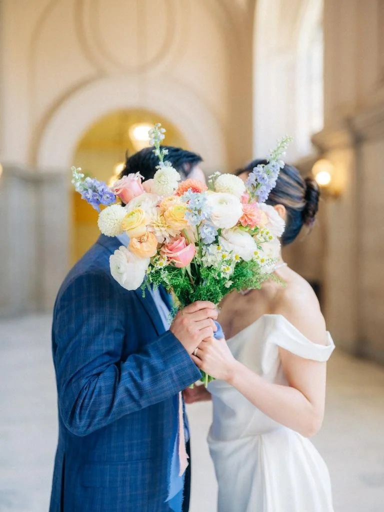 Bride and groom kissing behind her bouquet during portraits at San Francisco City Hall.