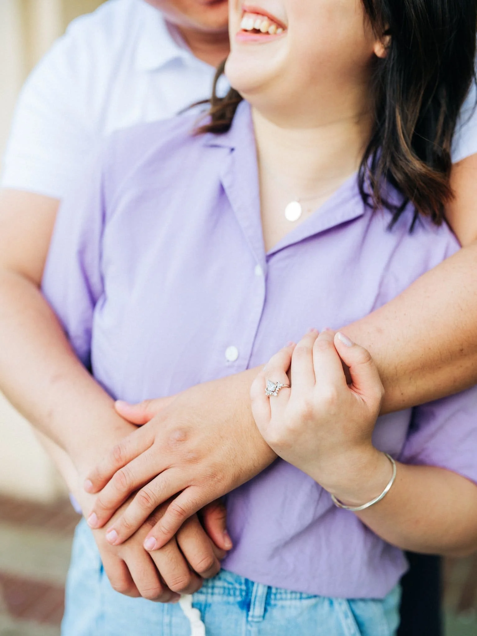 Groom-to-be embracing the bride-to-be from behind during their Montalvo Arts Center engagement photos in Saratoga, with her engagement ring visible.