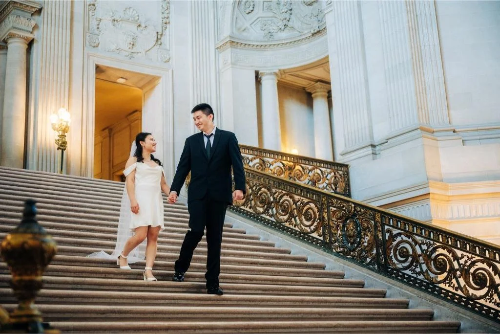Bride and groom holding hands and looking at each other while walking down the City Hall stairs