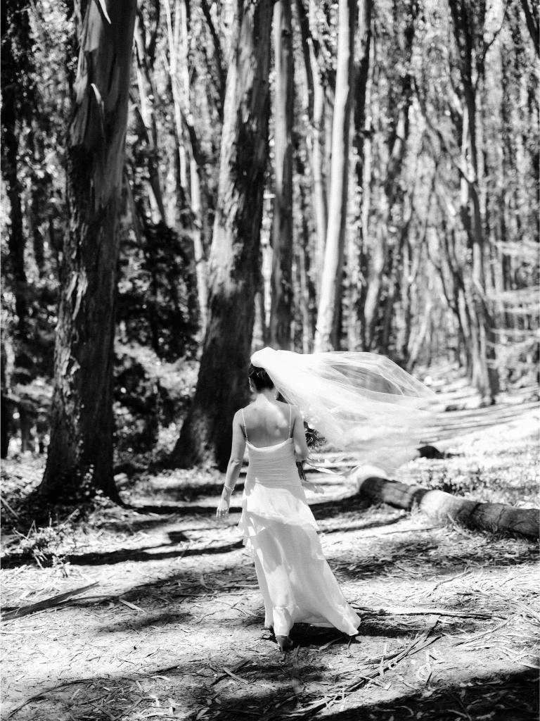 Bride walking along a wooded path at Lover's Lane as her veil flows in the wind.
