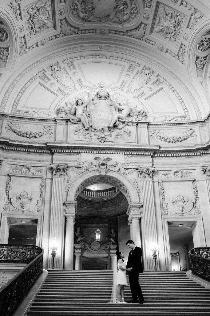 Bride and groom holding hands and looking at each other at the bottom of the grand staircase