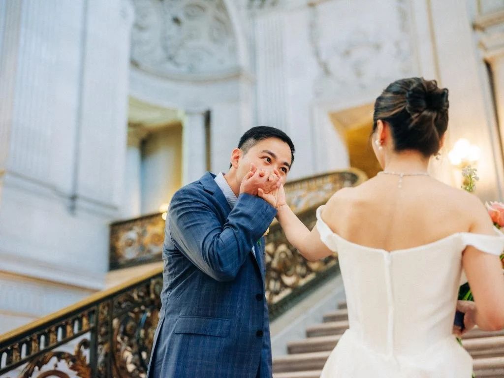 Groom kissing the bride's hand at the bottom of the San Francisco City Hall grand staircase.