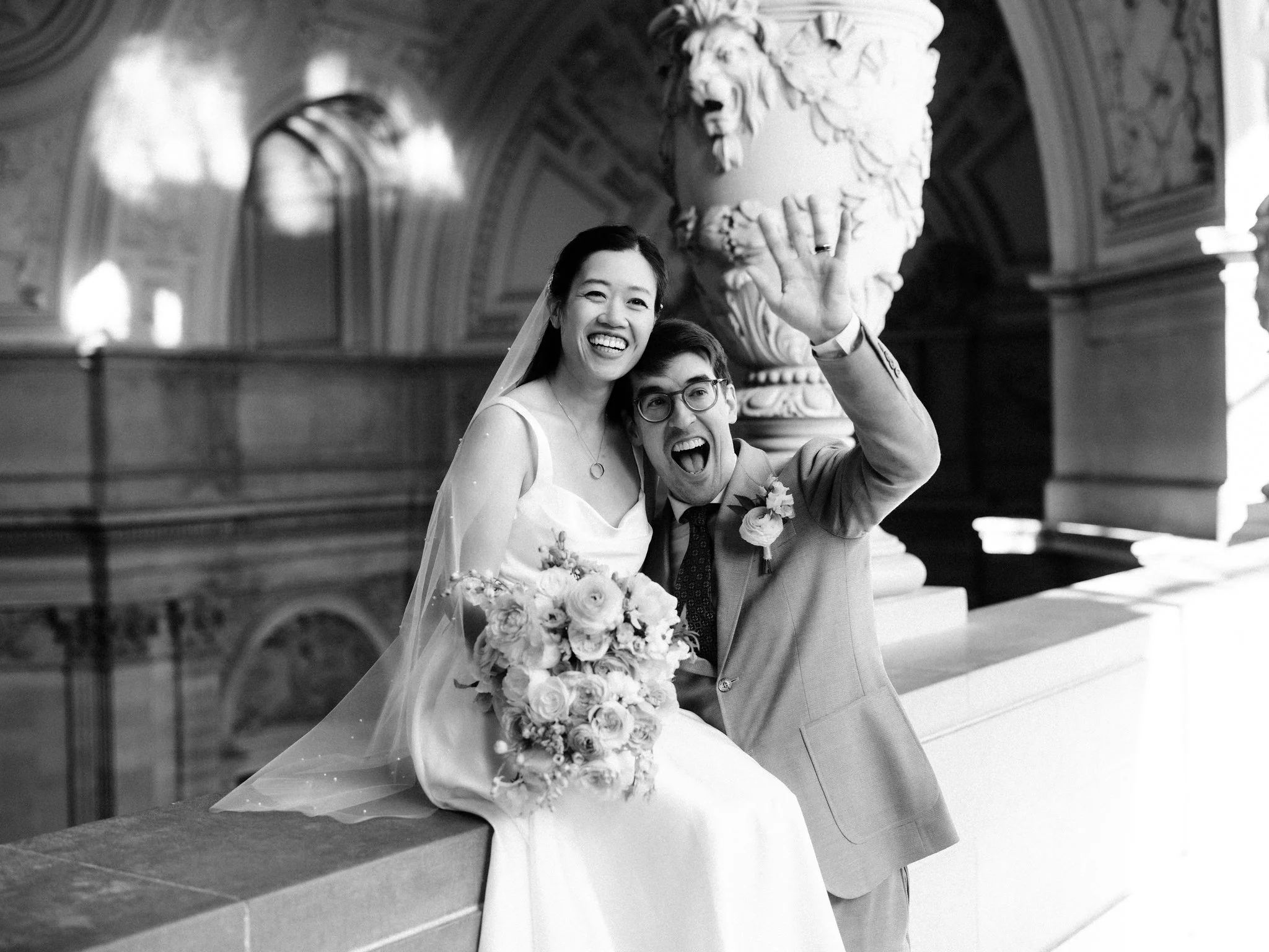 Bride sitting on balcony while groom waves at San Francisco City Hall wedding