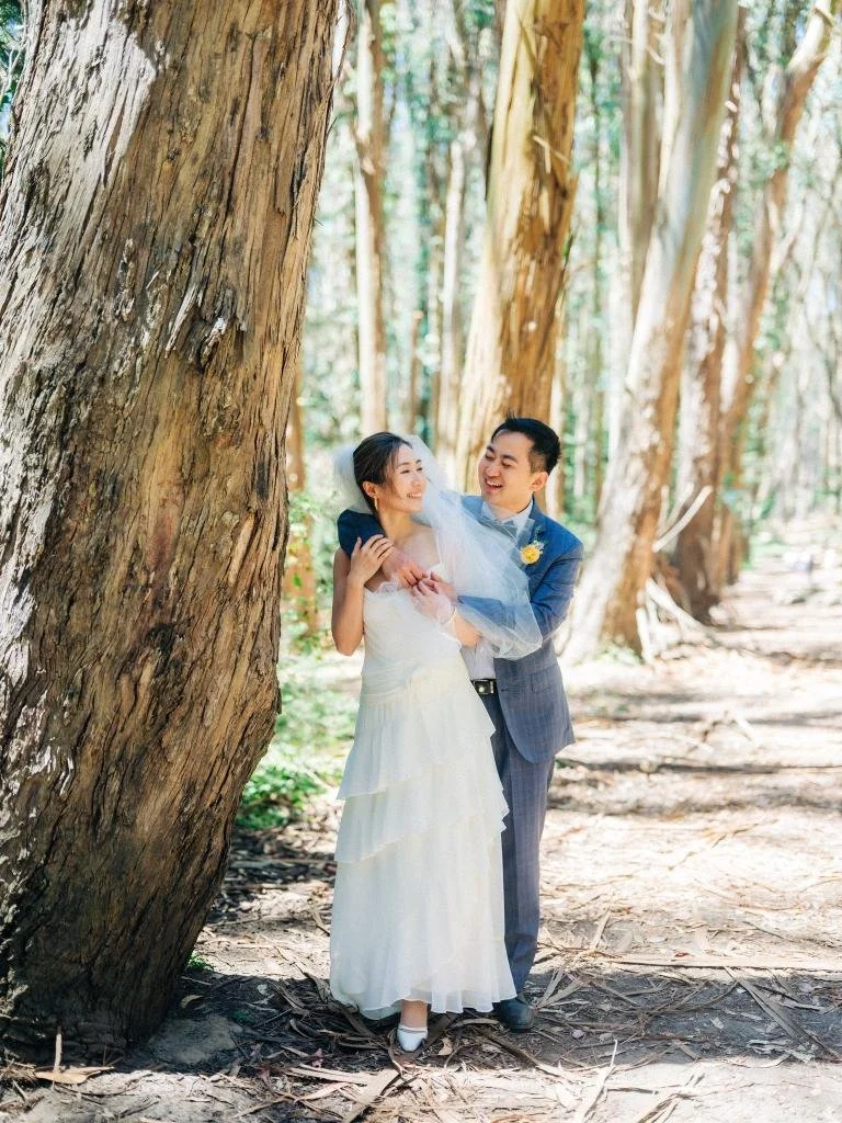 Groom embracing the bride from behind beside a tree during their Presidio elopement portraits.