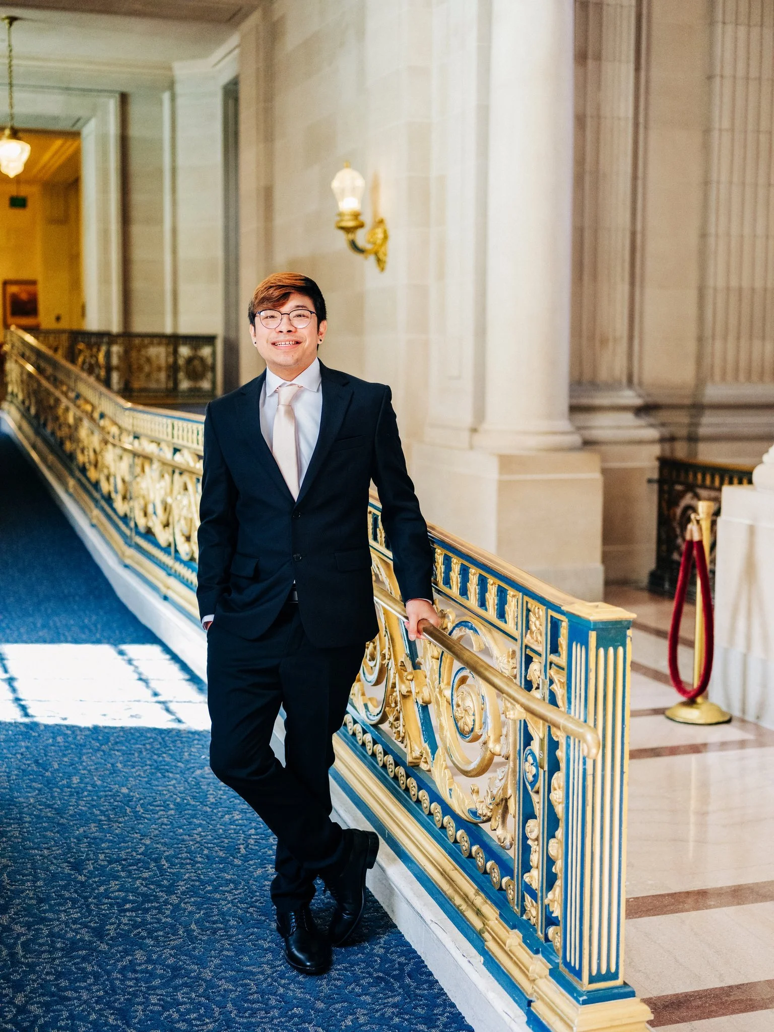 Groom posing beside iconic gold railing at San Francisco City Hall wedding