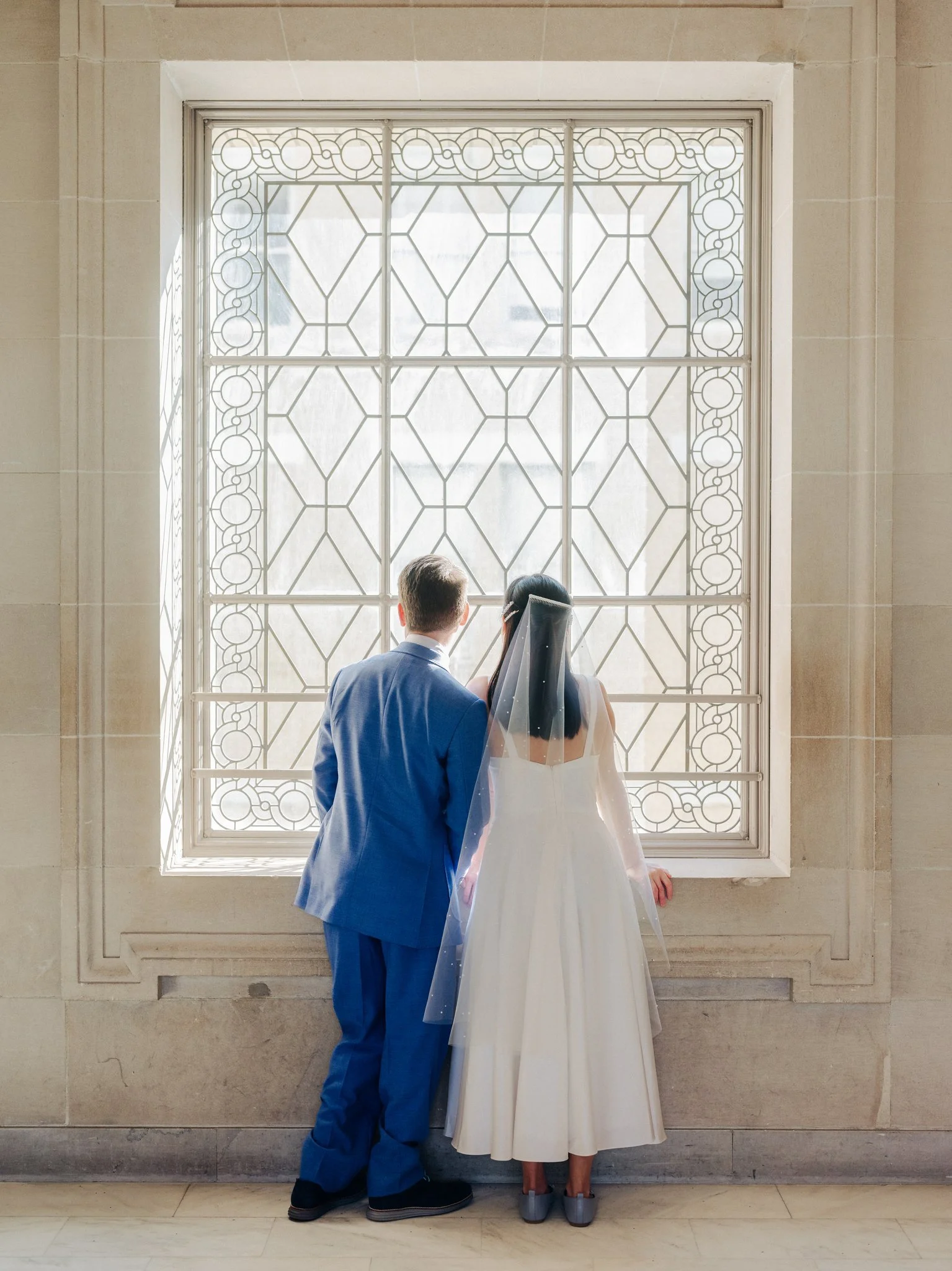 Bride and groom looking out stained glass window at San Francisco City Hall wedding