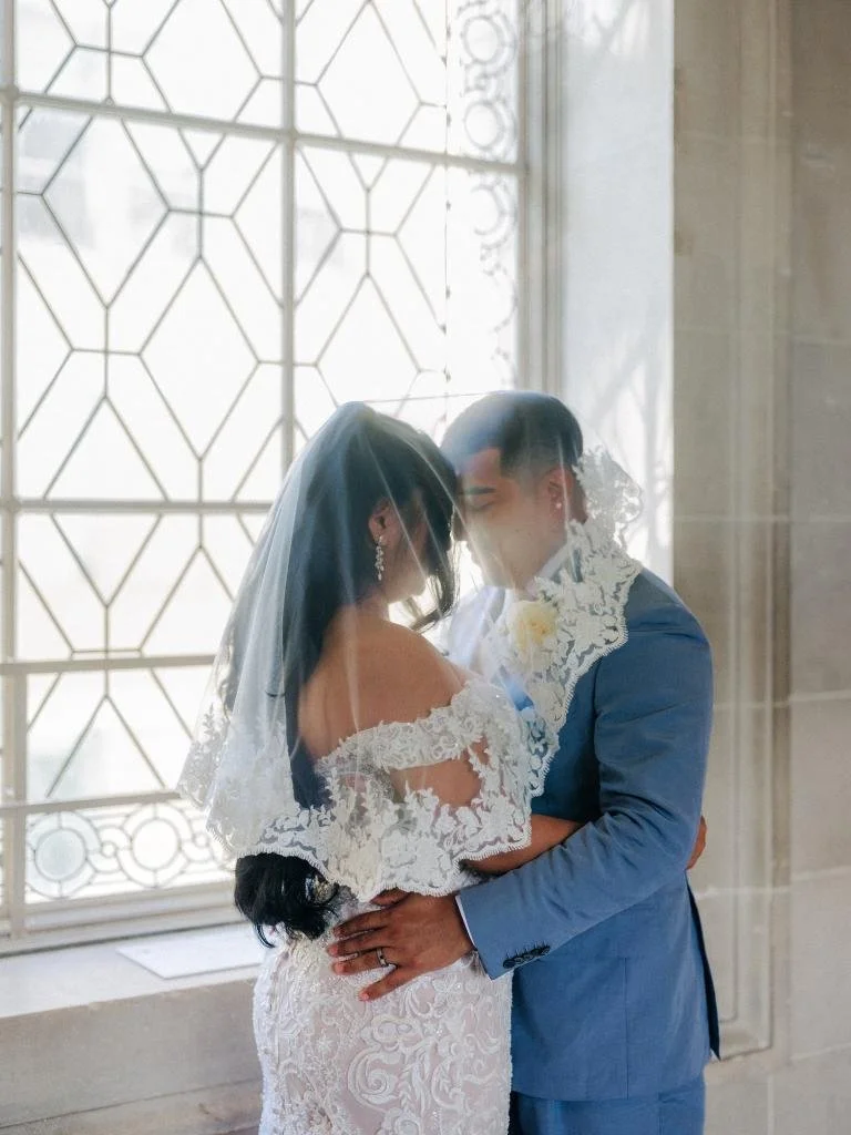 Bride and groom embracing in front of the stained glass window.