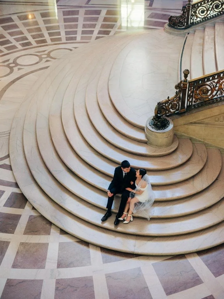 Overhead view of the bride and groom sitting together at the bottom of a City Hall stairwell