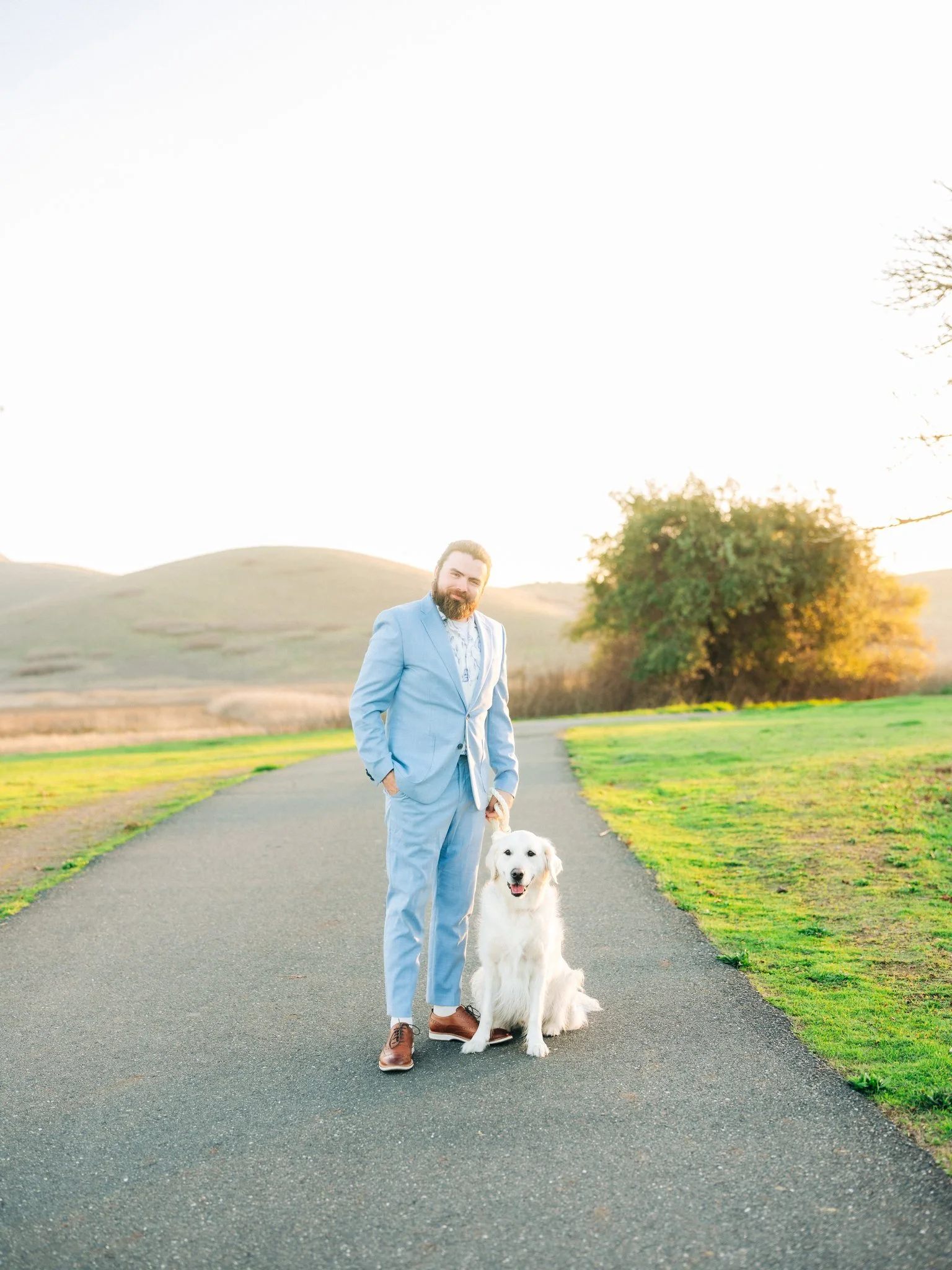 Man in a suit holding a dog on a leash during a couples photo session at Coyote Hills Regional Park in Fremont CA