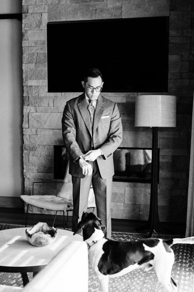 Groom adjusting his suit sleeve while his dog watches