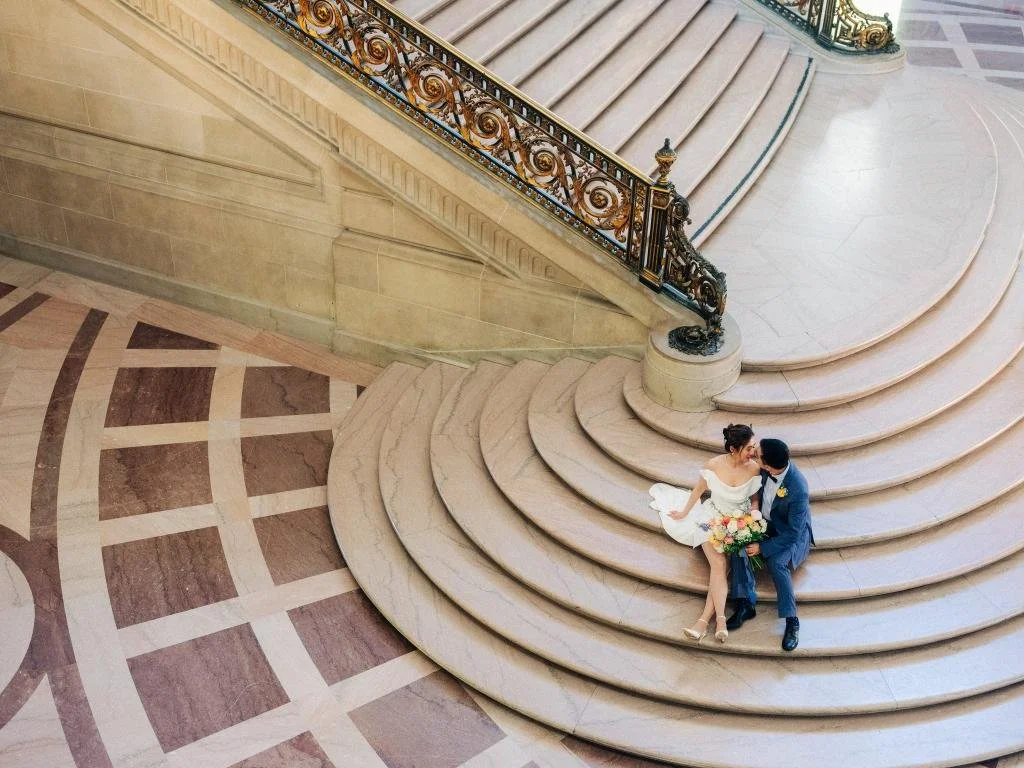 Overhead view of the bride and groom sitting together at the bottom of the stairs inside San Francisco City Hall.