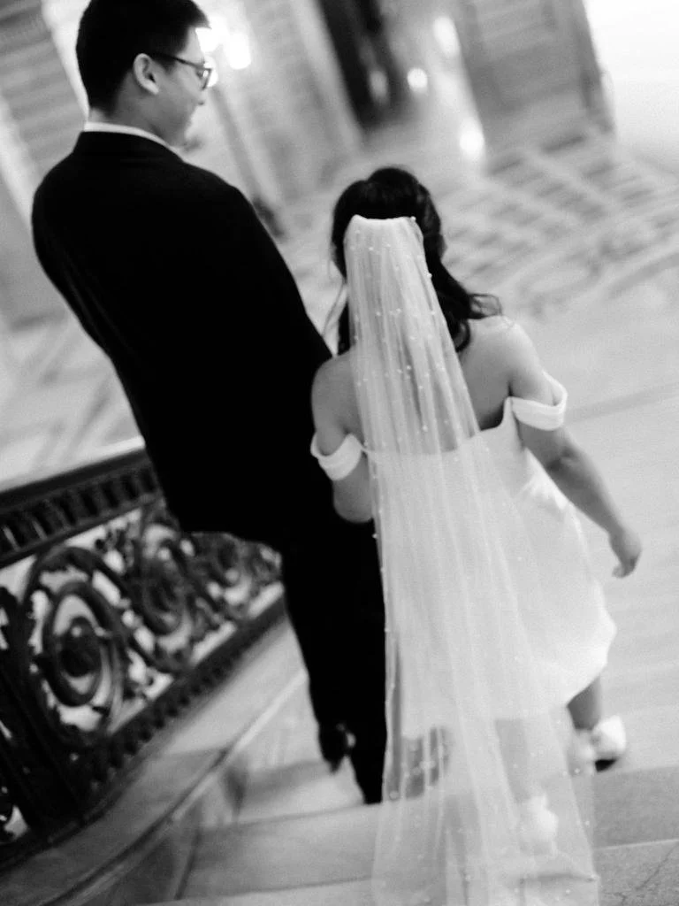 Bride and groom holding hands while walking down the City Hall stairs, photographed from behind