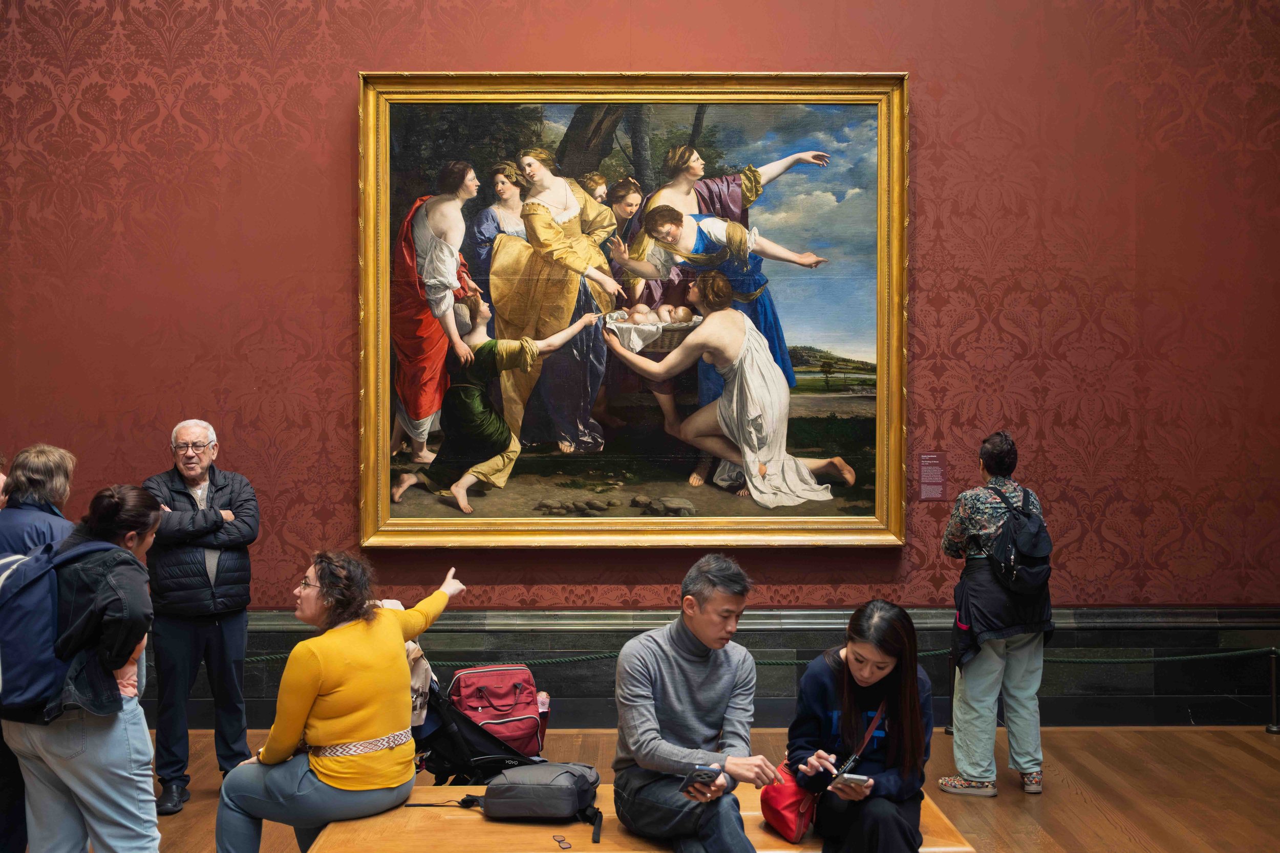 People viewing and discussing a large, framed painting in an art museum