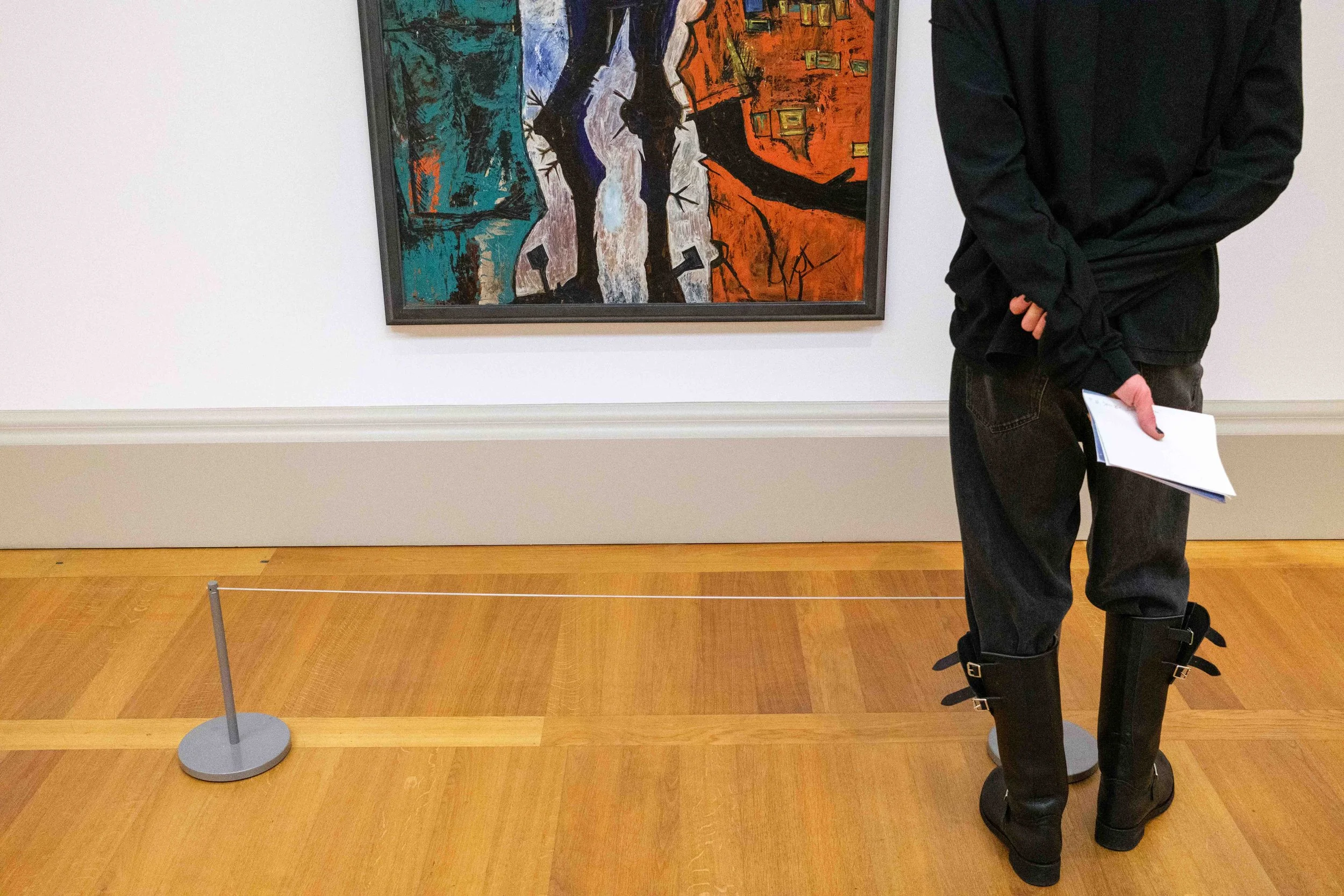 Person standing in front of an abstract painting at an art gallery, holding a notebook, with a barrier in front of the painting.