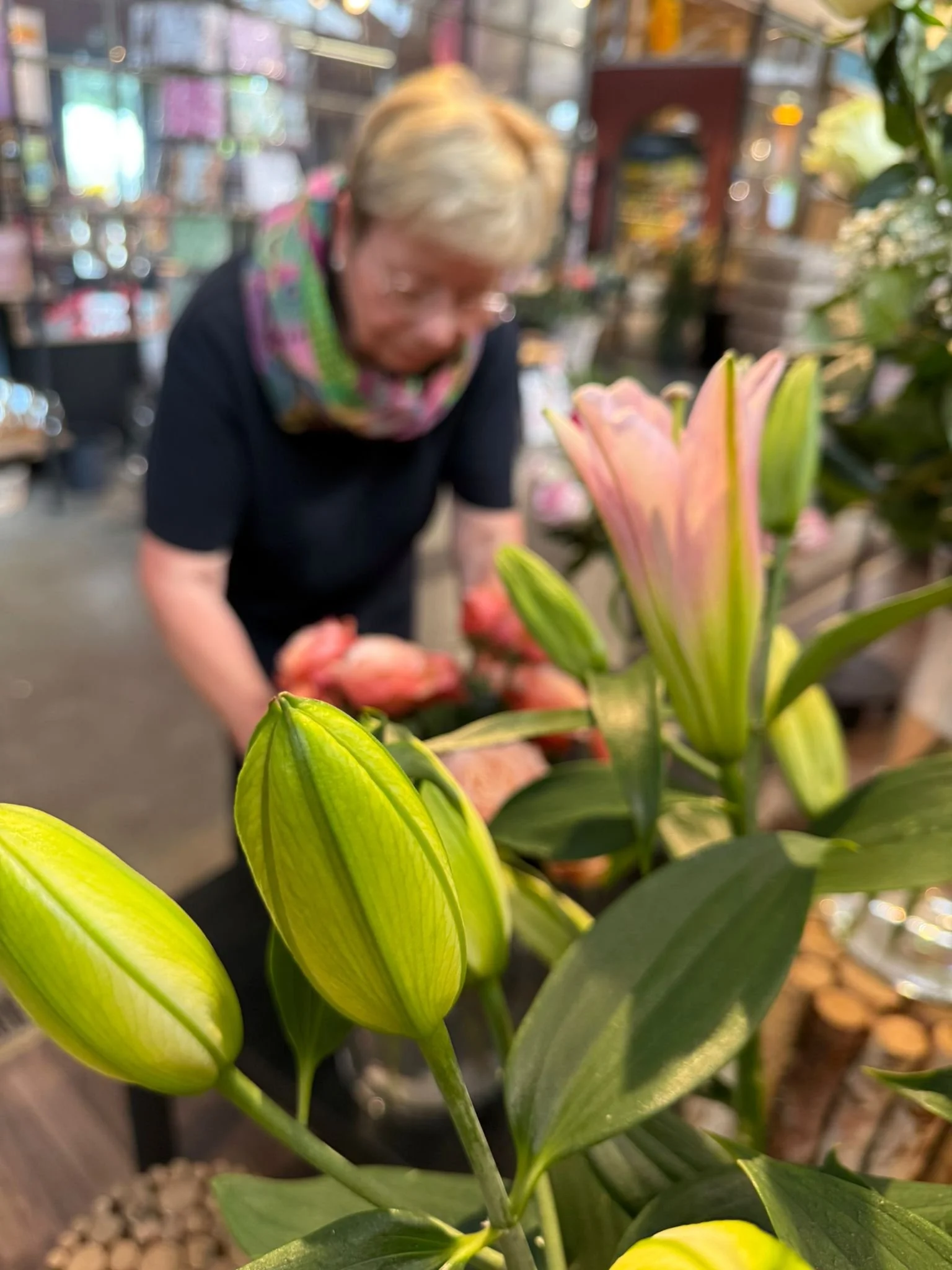 Nahaufnahme von blühenden Lilien im Vordergrund, im Hintergrund eine Frau in einem Blumengeschäft, unscharf