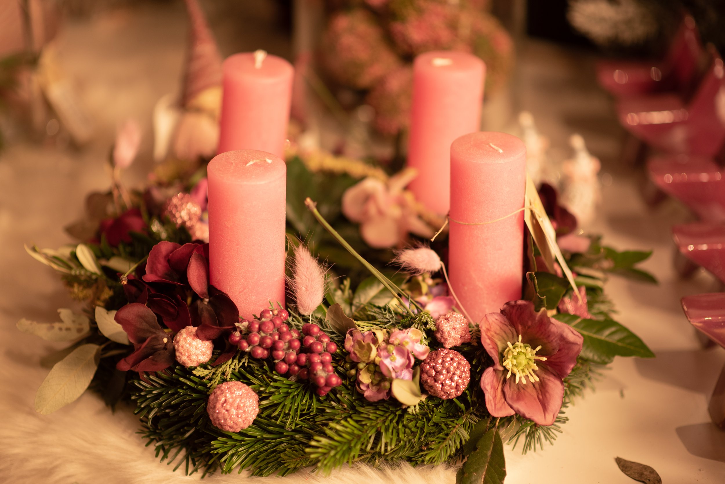 Eine Advents- oder Weihnachtsdeko mit vier rosa Kerzen und verschiedenen roten, pinken und weißen Blumen und Dekorationen auf einer Tanne