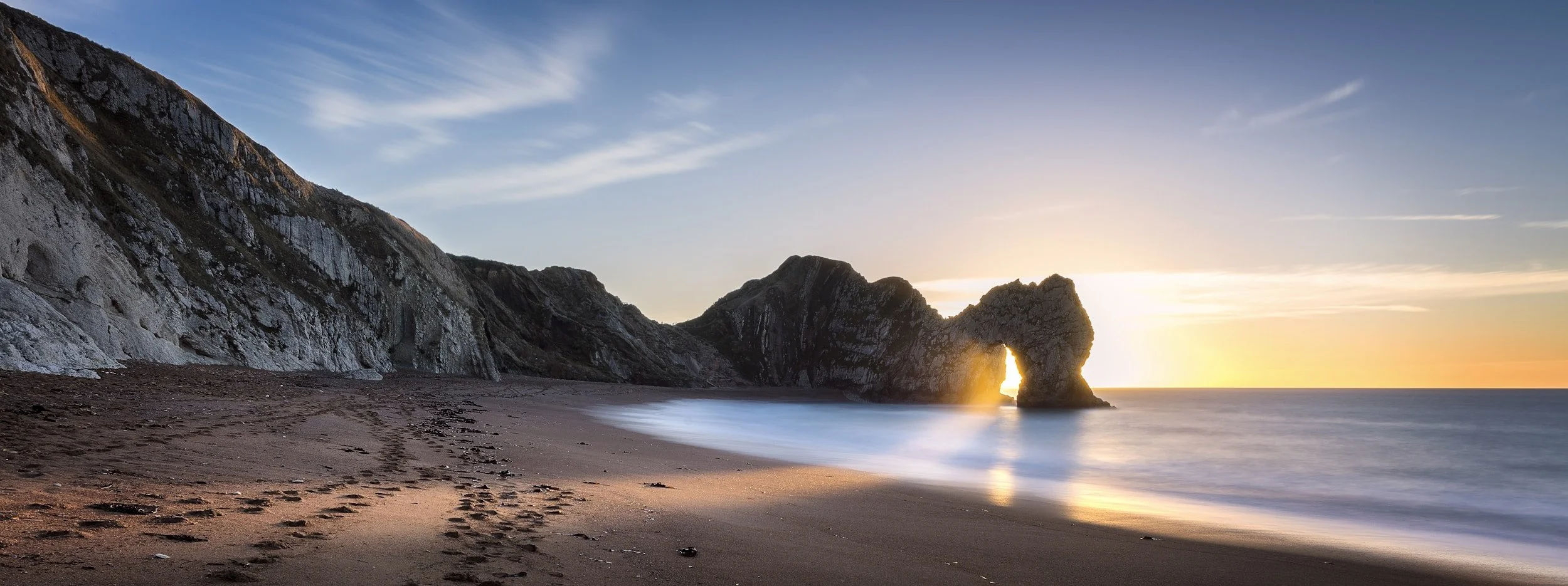 Sun rising through the arch of Durdle Door in Dorset