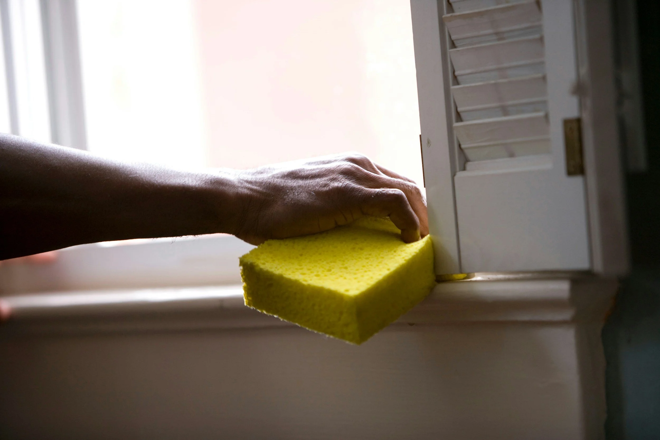 A person cleaning a window sill with a yellow sponge.