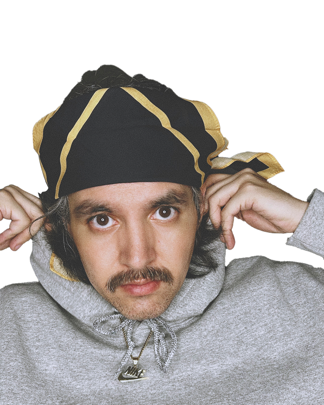 A young man with dark hair, mustache, and light skin wearing a gray hoodie and a black bandana with gold accents, adjusting it with both hands, and looking directly at the camera.