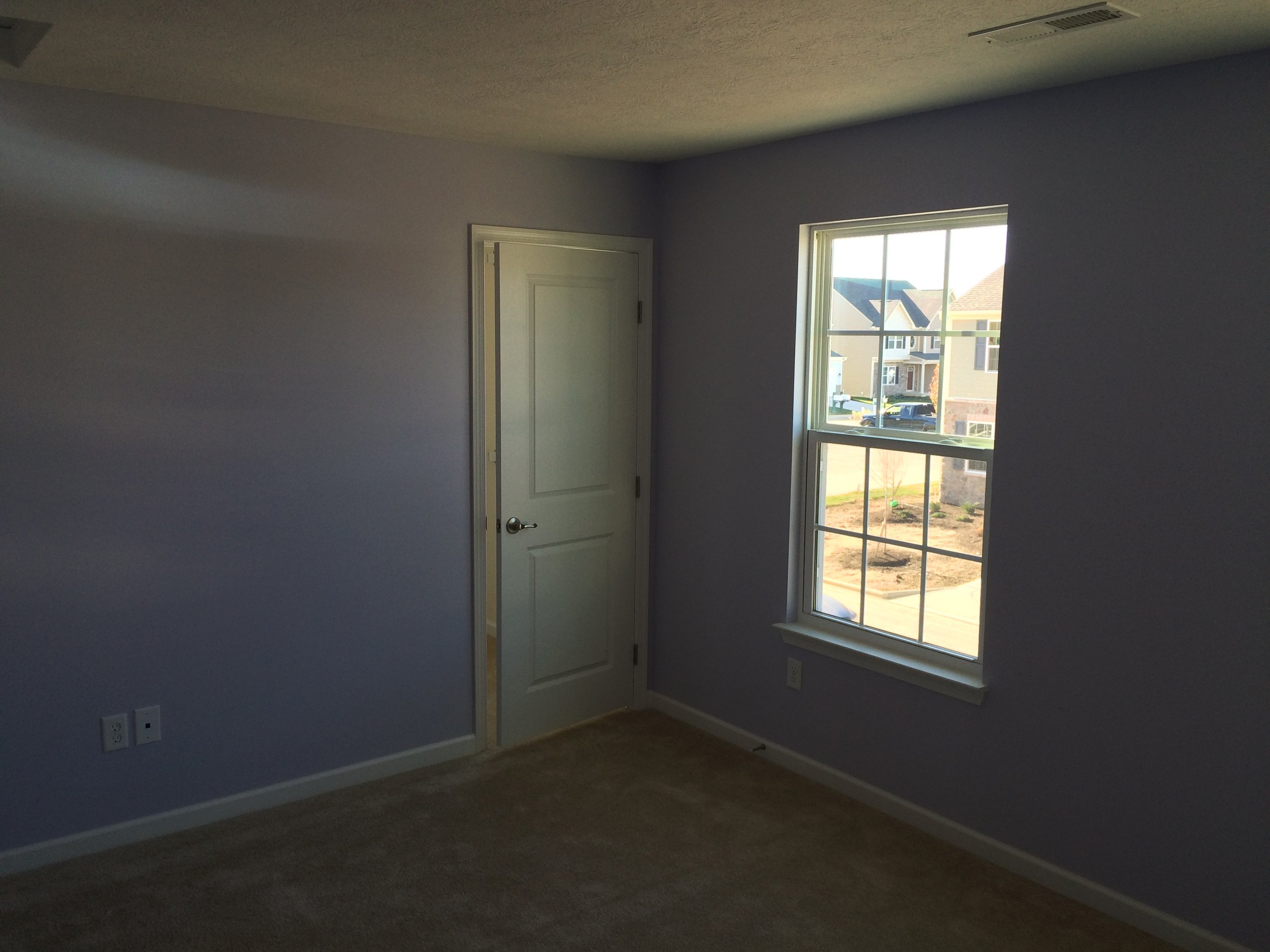 Empty room with a window showing a neighborhood outside, and a closed door on the wall.