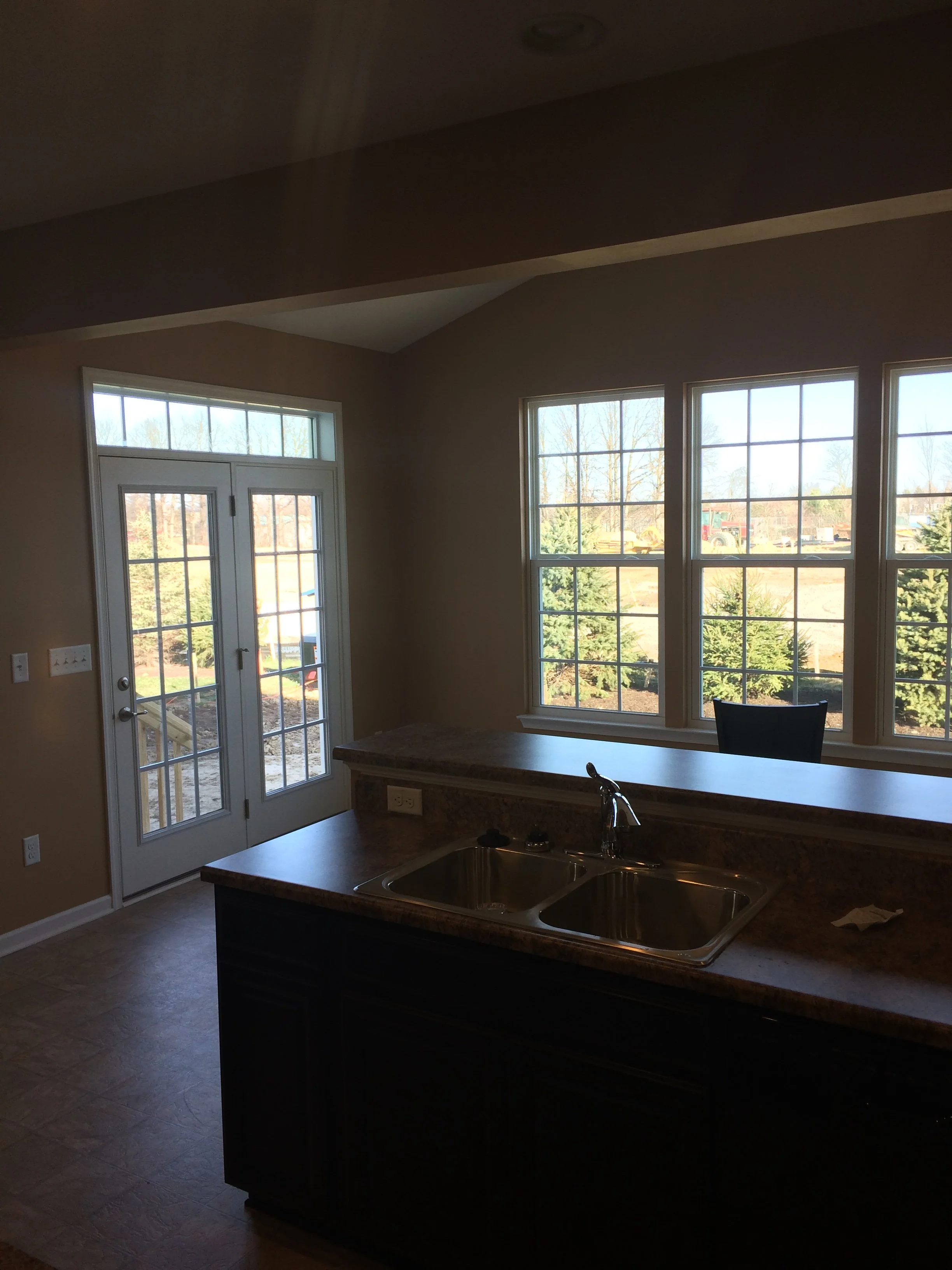 A kitchen with large windows letting in natural light, a granite countertop with a double sink, and a set of French doors leading outside.