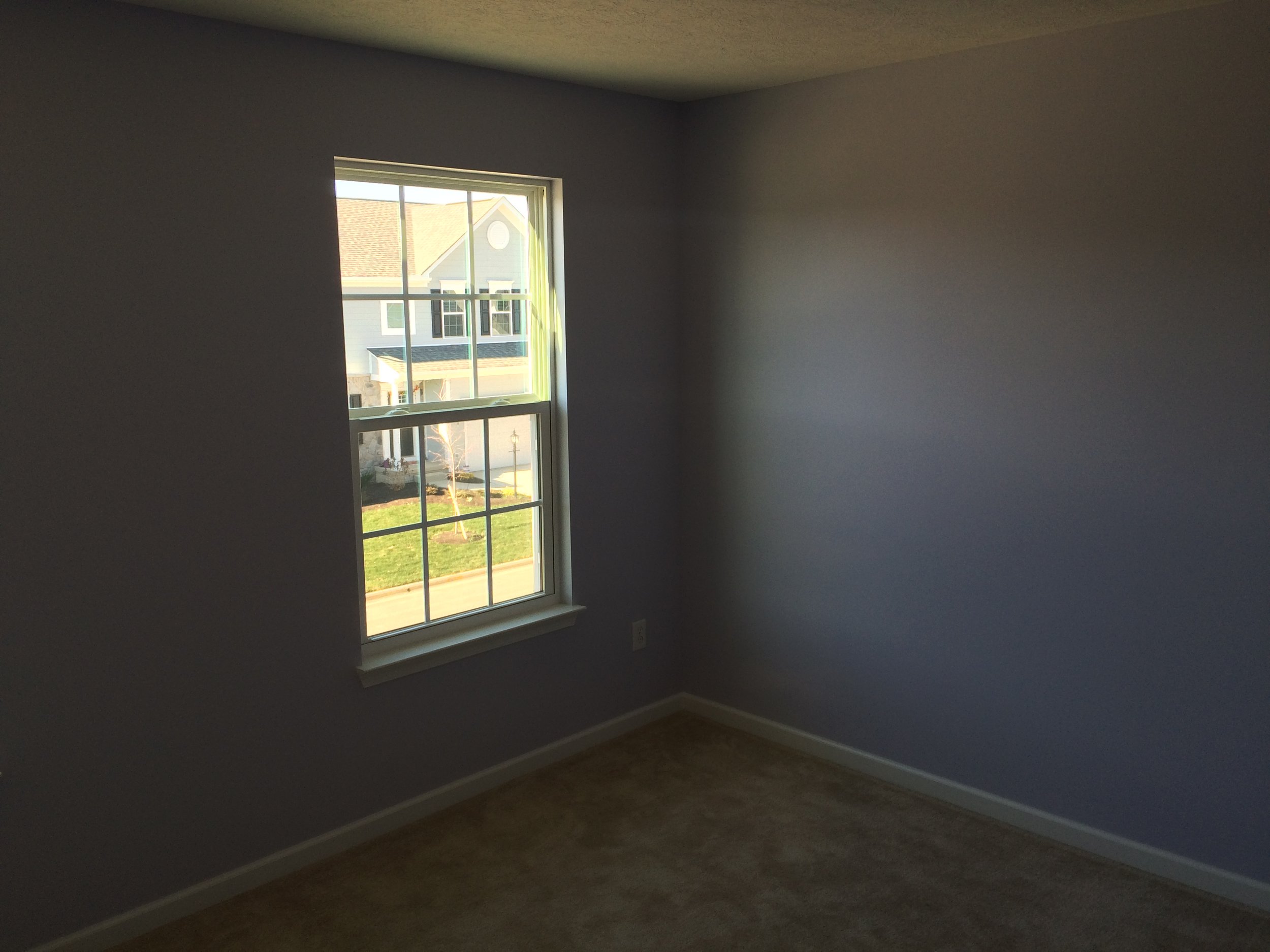 Empty room with gray walls, a window showing houses outside, and a hardwood floor.