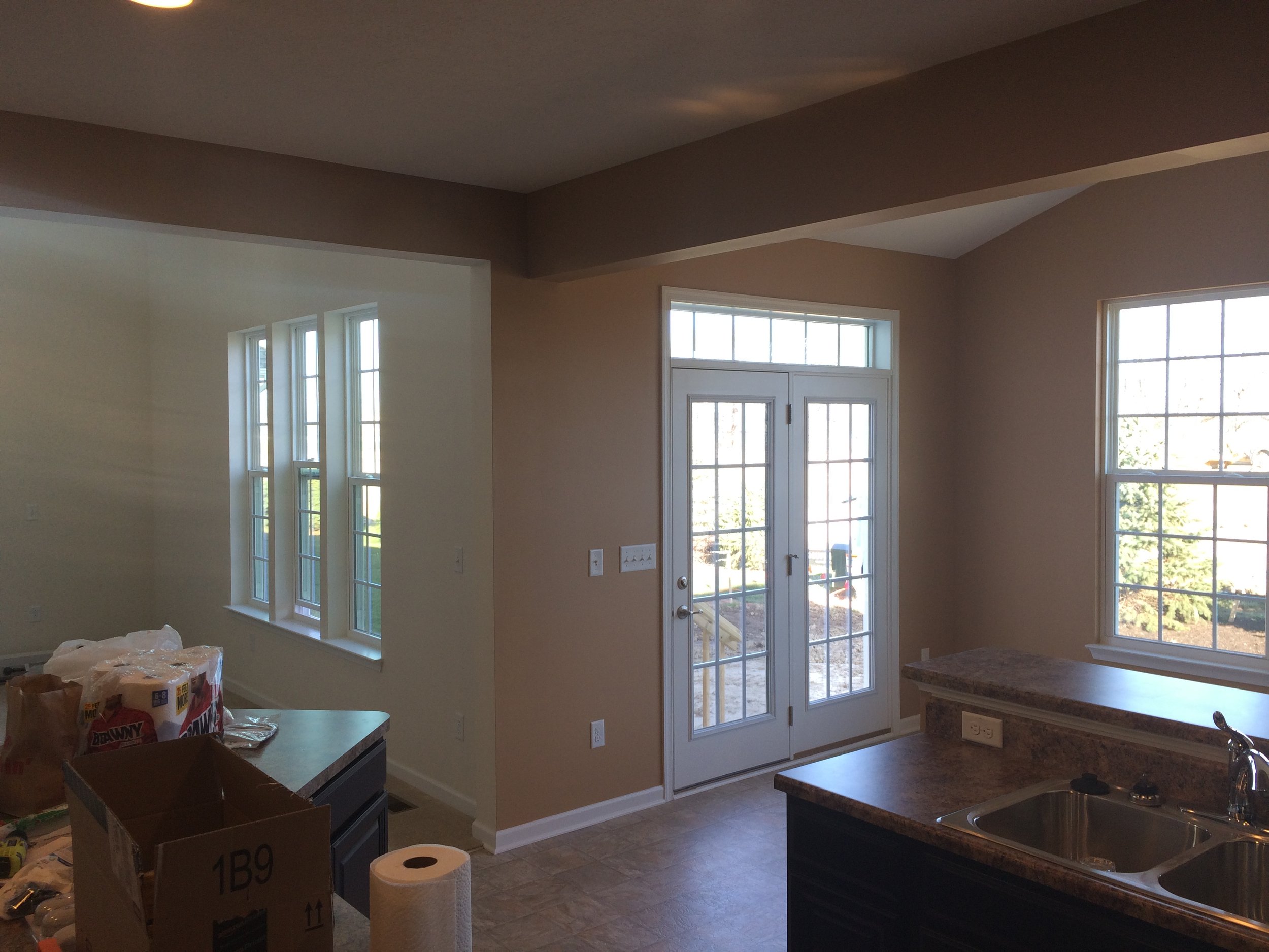 A kitchen with large windows and a glass door, beige walls, and a granite countertop. There are boxes and paper towels on the counter, indicating ongoing room setup or renovation.