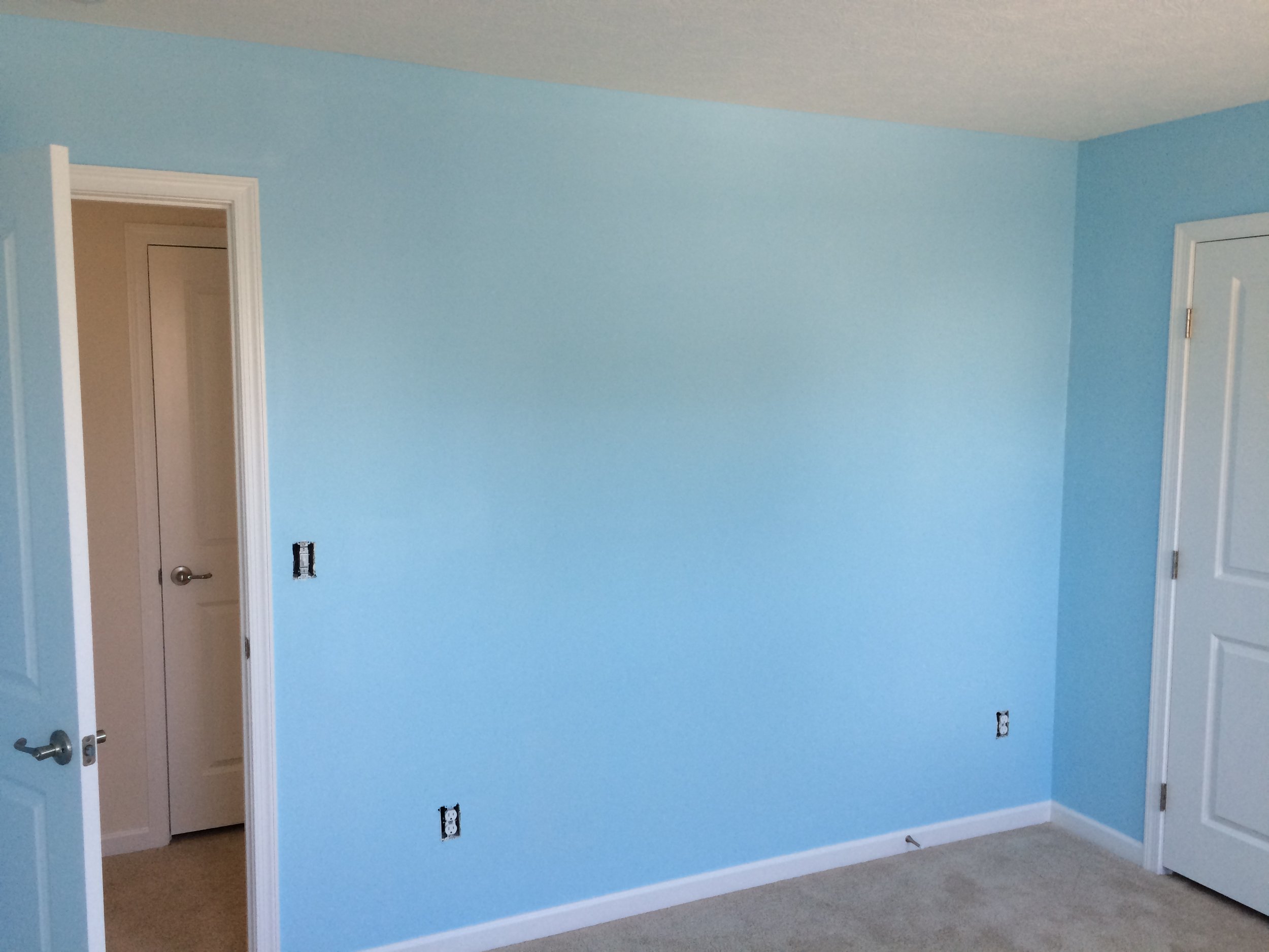 A room with light blue painted walls, two open white doors, and electrical outlets on the wall. The room appears to be under renovation or construction.
