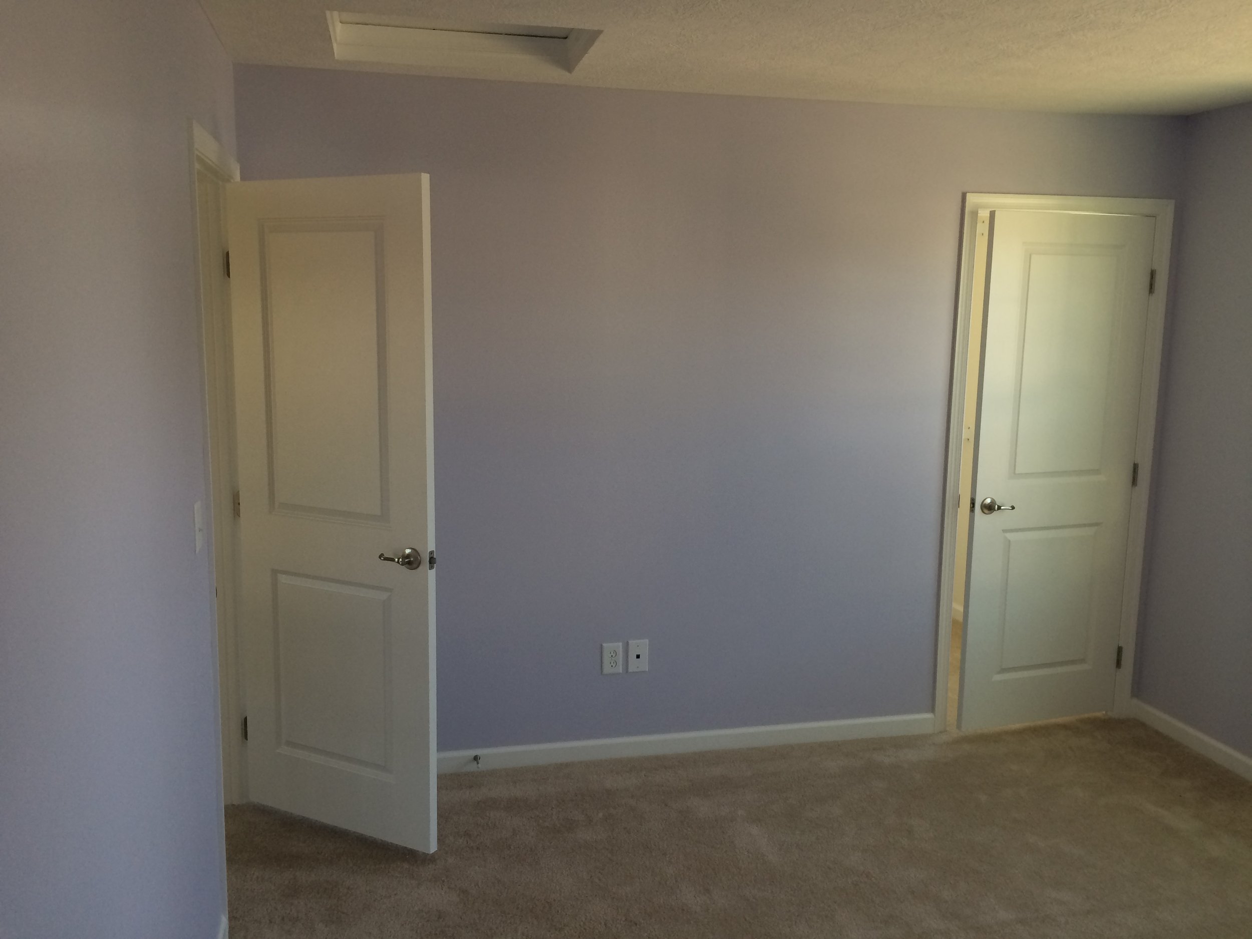 Empty room with beige carpet, light gray walls, two closed white doors, and electrical outlets on the wall.