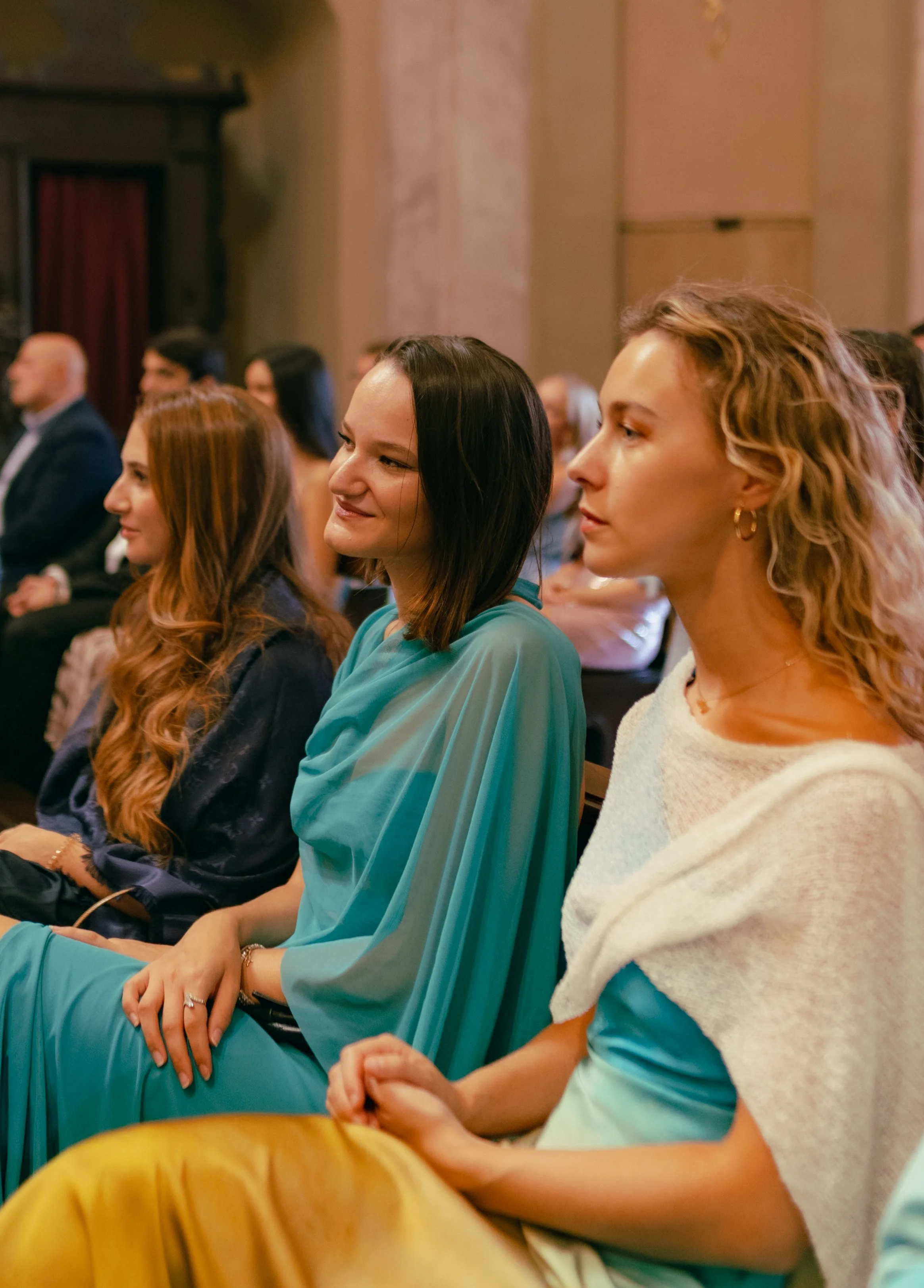 People sitting attentively at an indoor event or conference, with some smiling and listening.