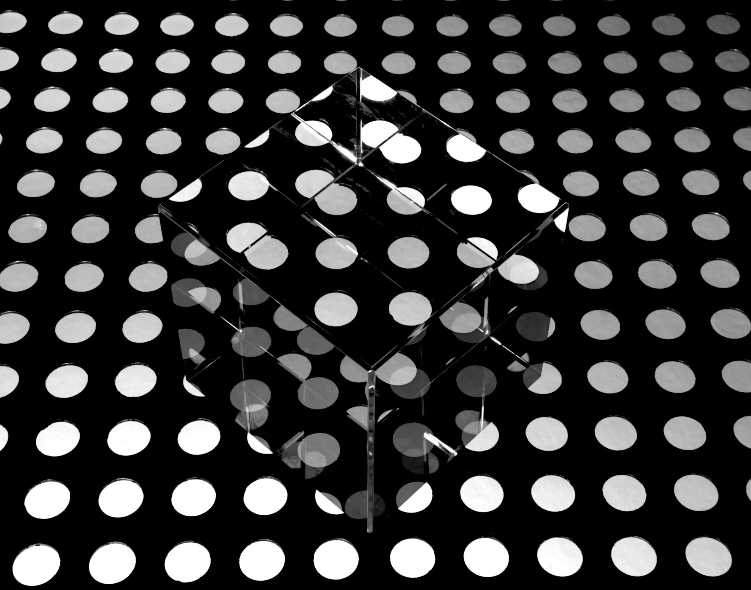 An abstract black and white image featuring a transparent glass cube over a polka dot pattern, representing layered complexity and the invisible structure of a web design project.