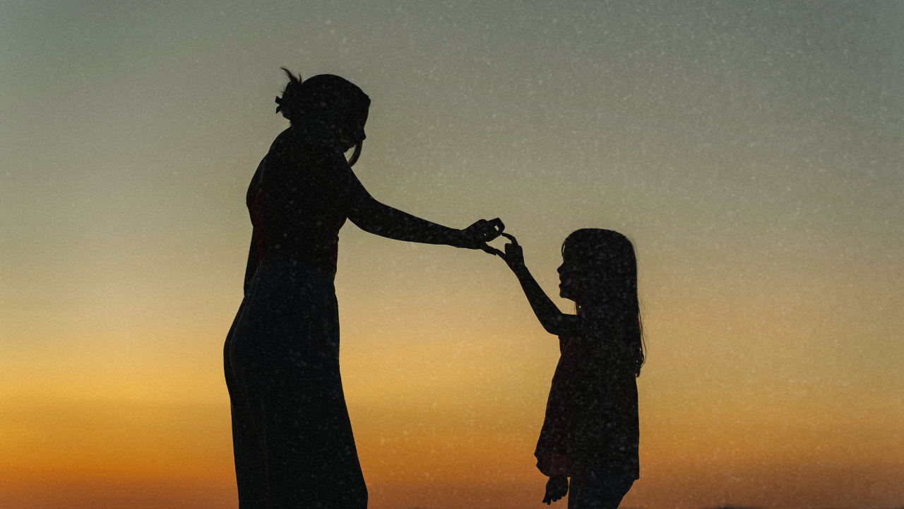 Silhouette of an adult reaching for a child at sunset, representing healing from childhood trauma and reconnecting with your younger self.