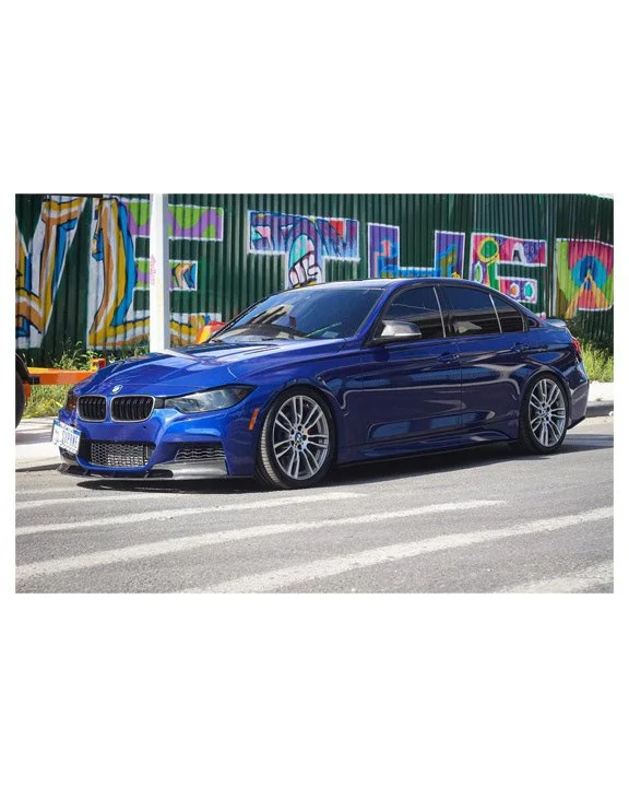Blue BMW sedan parked on city street in front of colorful graffiti wall.