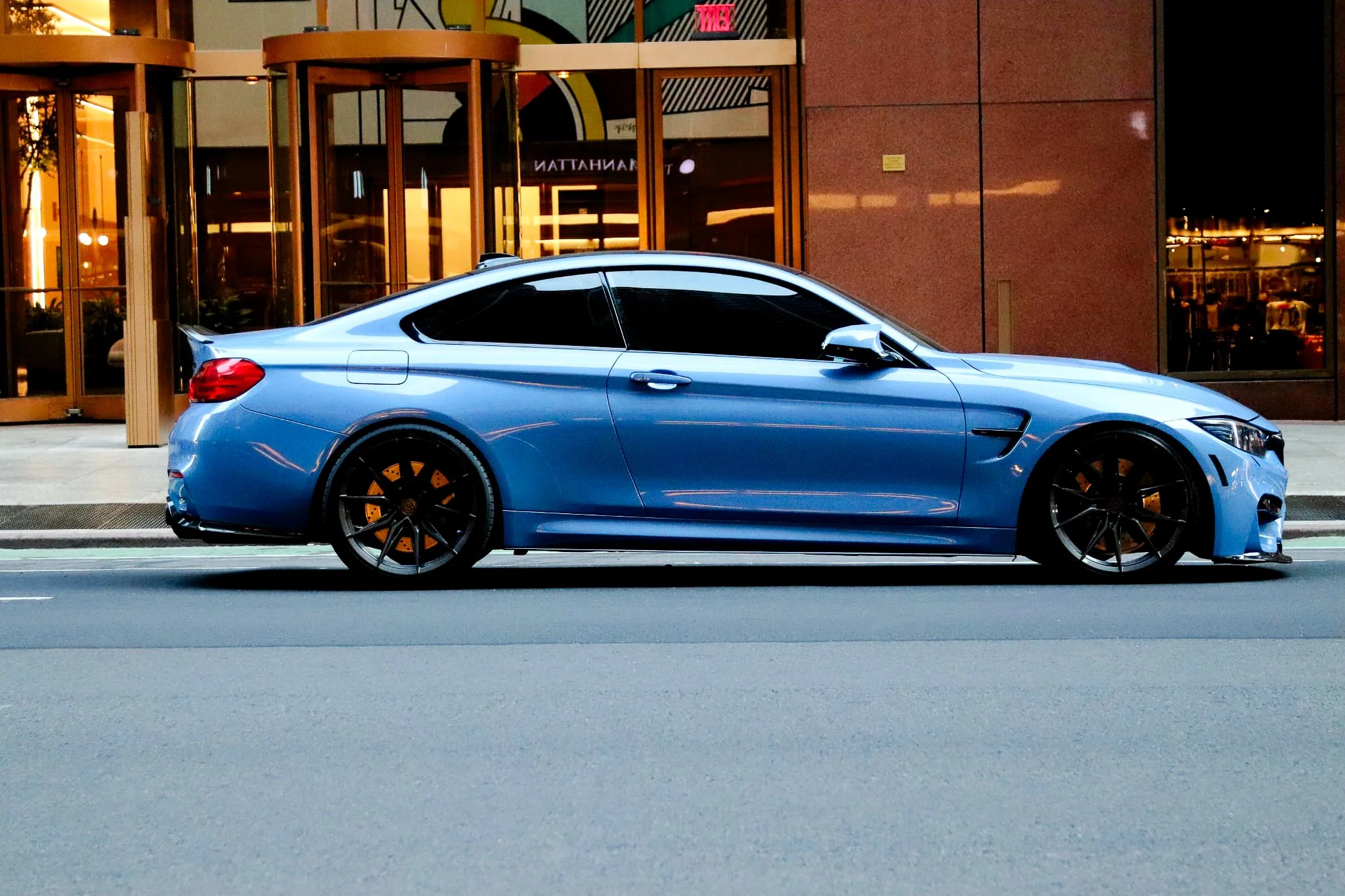 A blue luxury sports car with tinted windows parked on a city street at night, in front of a building with glass doors and windows.