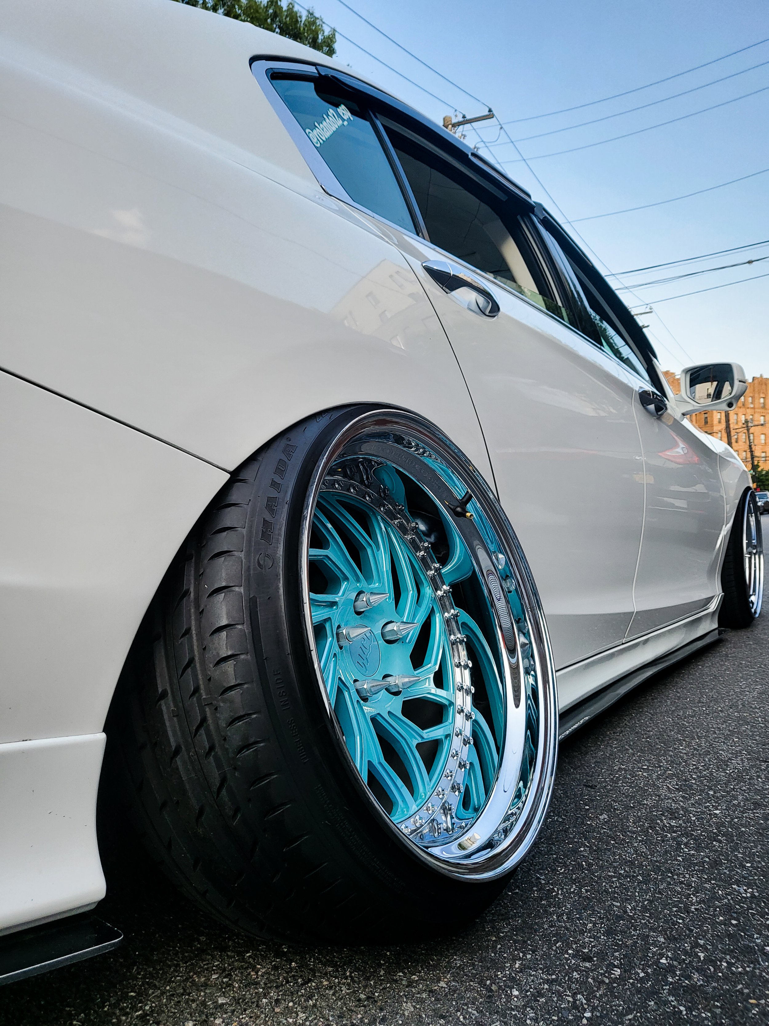 a white car with customized light blue and chrome rims parked on the street.