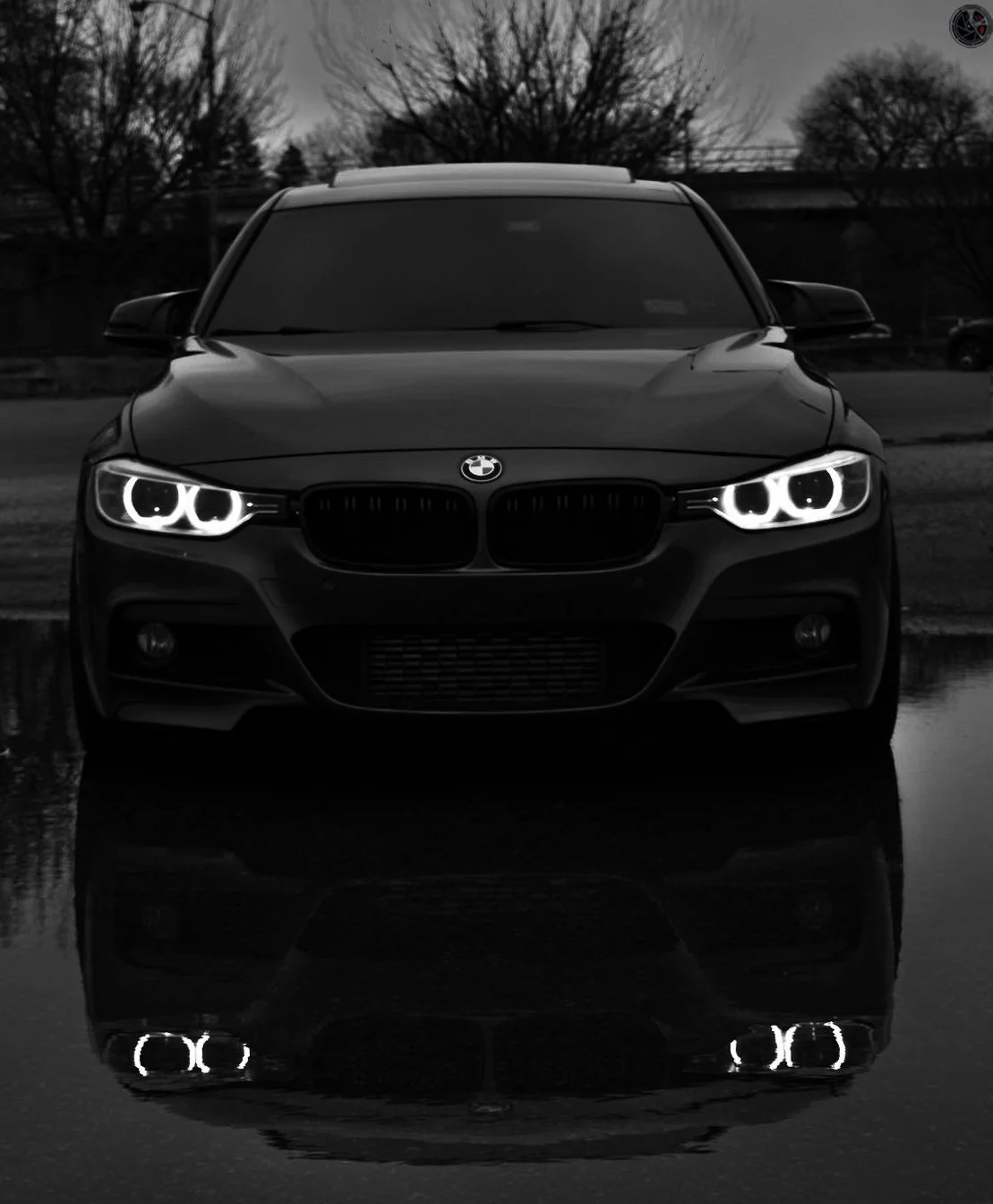 A black BMW car with glowing headlights, reflected on a wet surface.