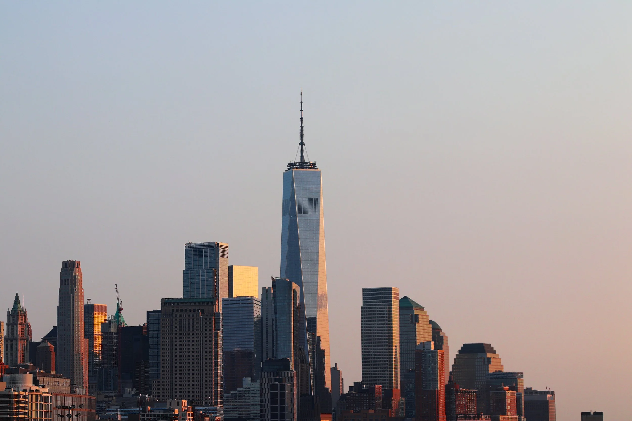 Skyline of New York City with One World Trade Center in the center, during sunset.