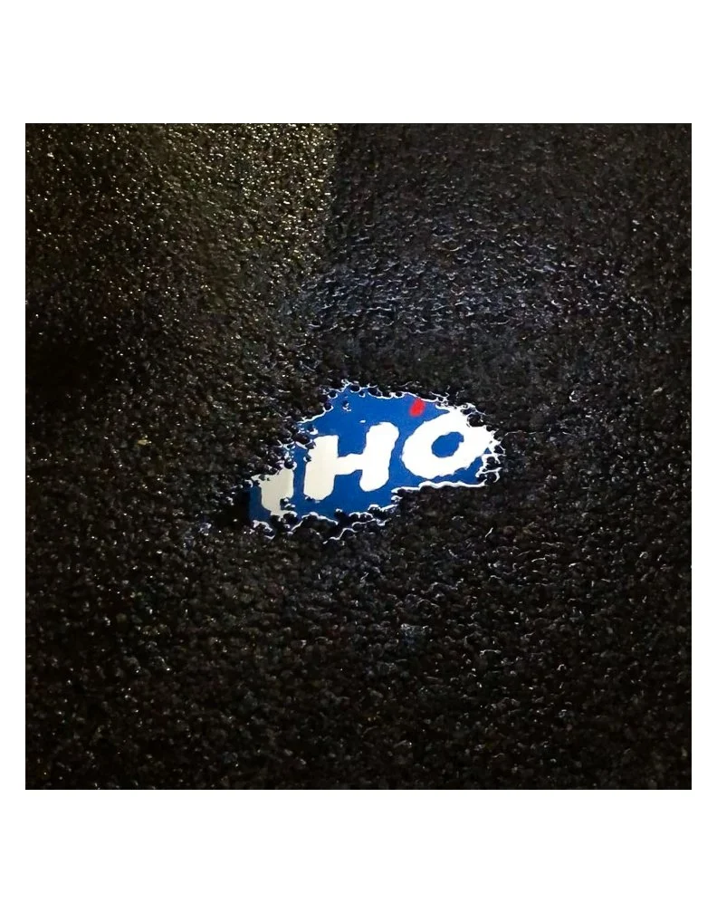 A puddle of water on a dark, textured surface reflecting a part of a sign with blue and white colors.