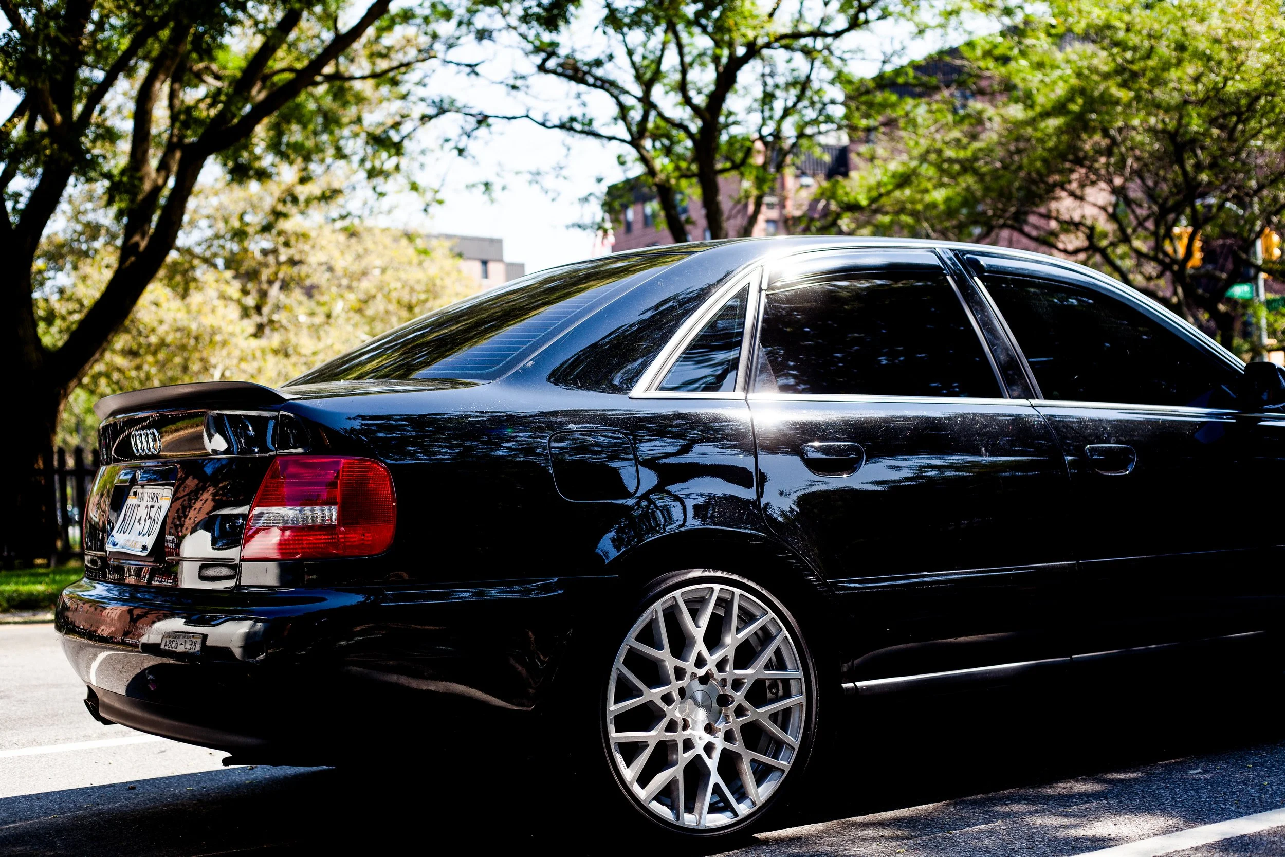 Black luxury sedan parked on street with trees and buildings in background.